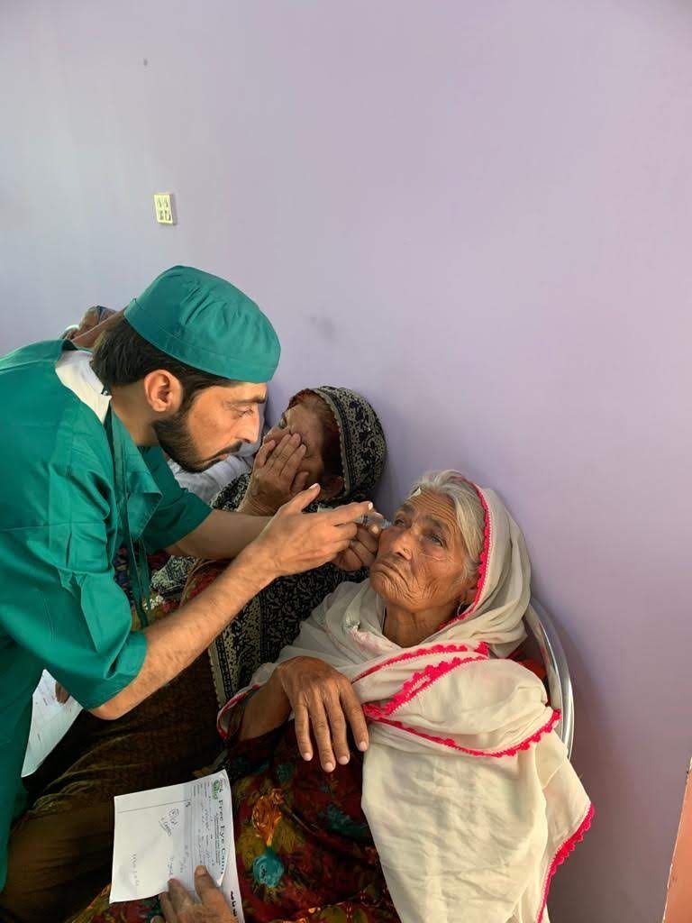 A doctor in surgical scrubs examines the eyes of an elderly woman at the 2019 camp