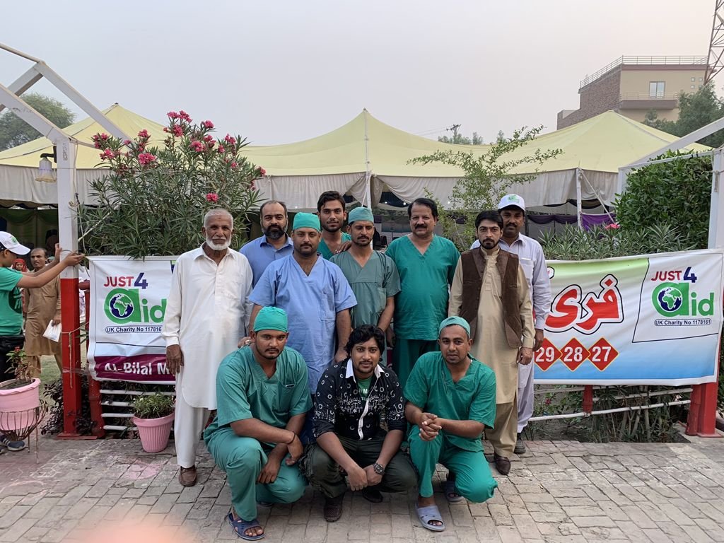 The Just4Aid team, volunteers and surgeons in green scrubs gathered in front of the camp banner in Sahiwal