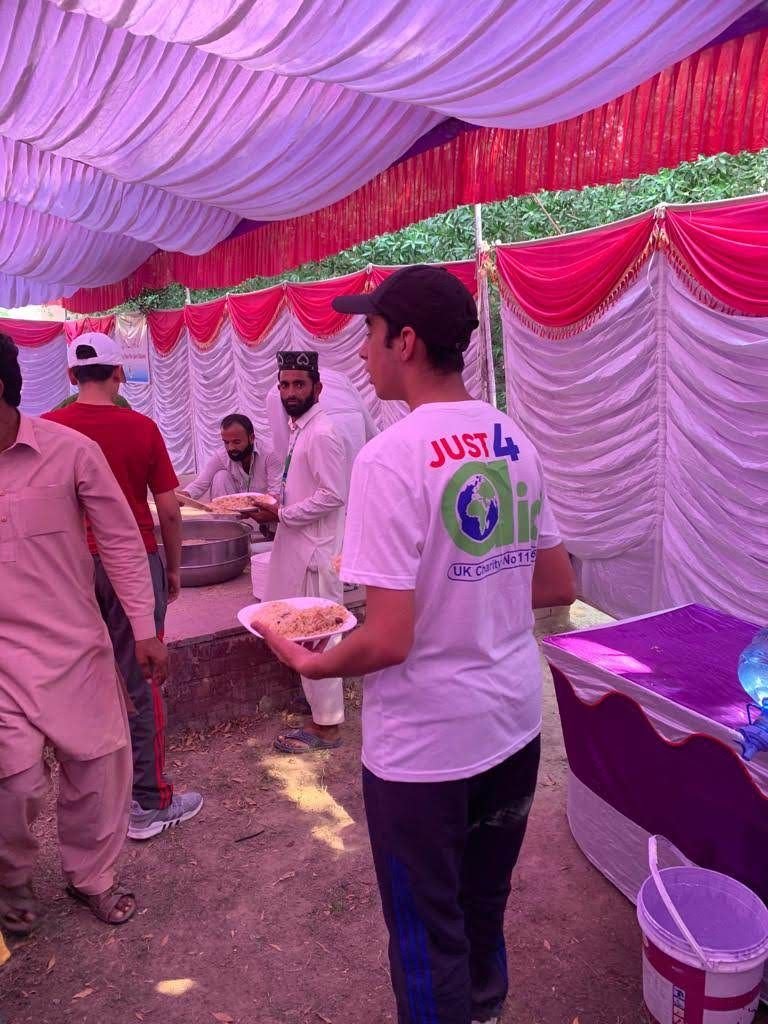 A volunteer in a Just4Aid T-shirt serves a plate of food under the marquee