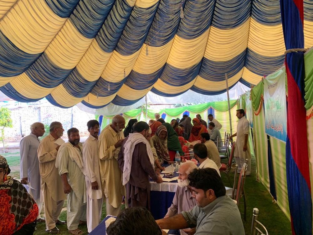 Volunteers at a registration desk under the marquee, with a queue of patients waiting