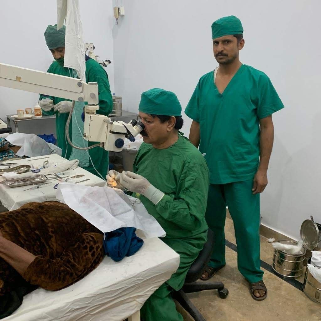 A surgeon operates using a surgical microscope while a colleague looks on