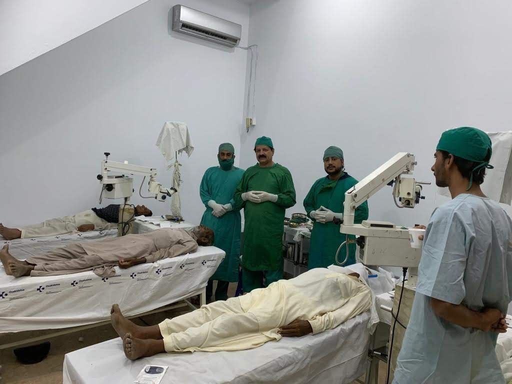 Surgeons in green scrubs beside patients resting after their operations